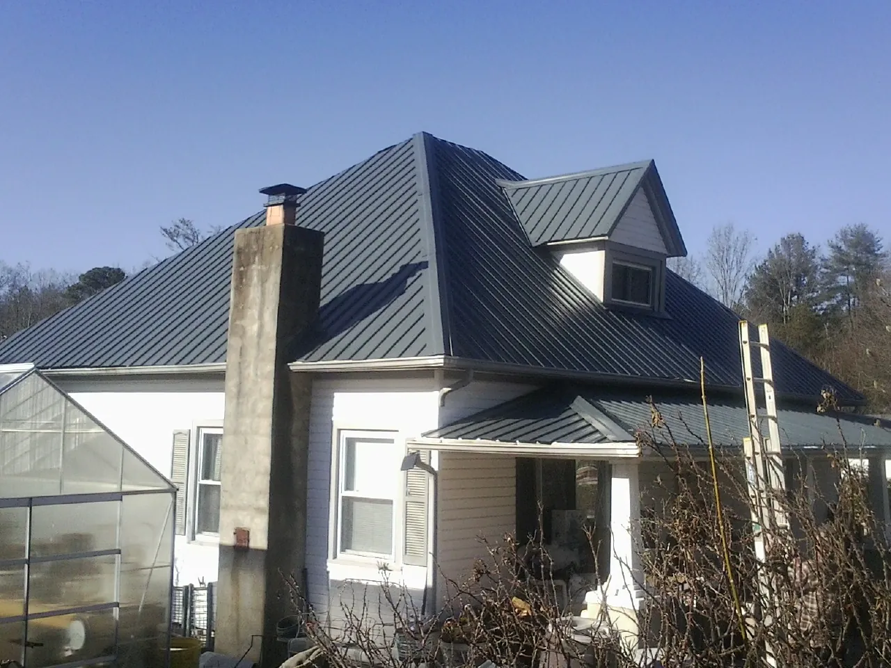 Dark blue standing seam metal roof on a white farmhouse with dormer — Slate & Tile Roof Repair by Roofing Brothers in Emporia