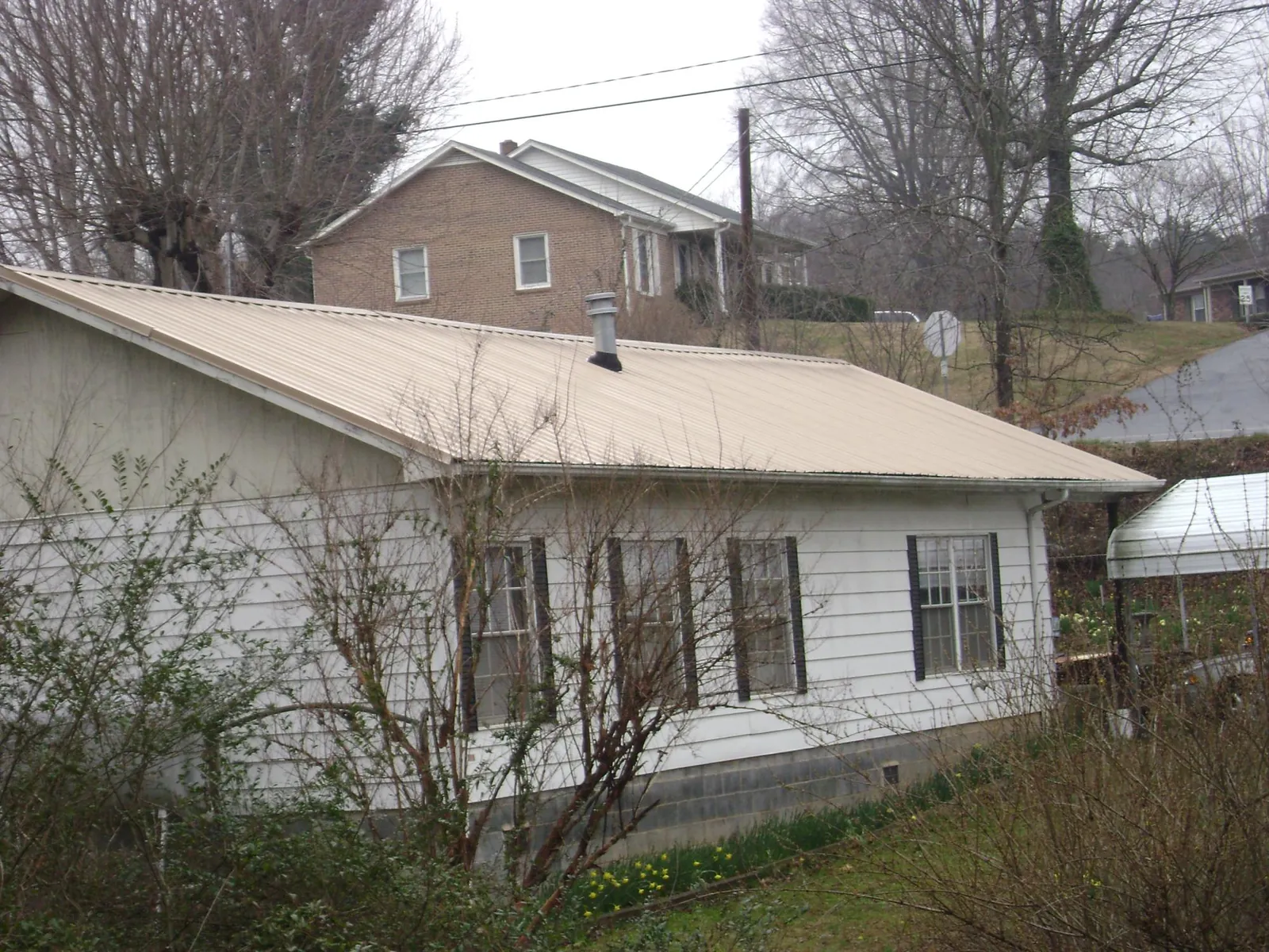 Tan metal roof on a white sided house set into a hillside — Commercial Roofing by Roofing Brothers in Emporia